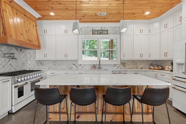 kitchen with white cabinetry, hanging light fixtures, a kitchen island, and range with two ovens