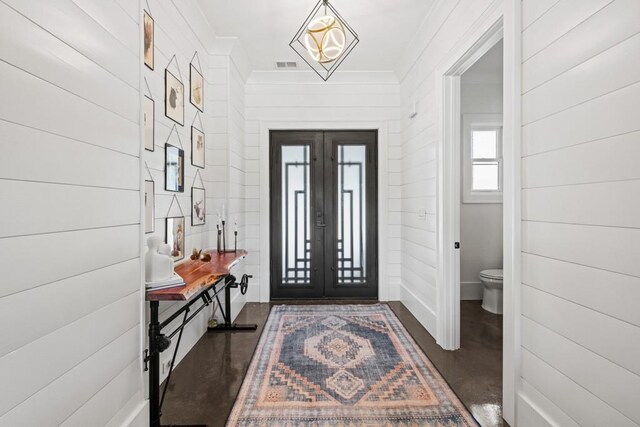 foyer with french doors, wooden walls, and crown molding