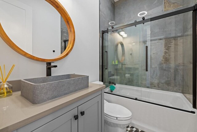 full bathroom featuring toilet, vanity, and bath / shower combo with glass door