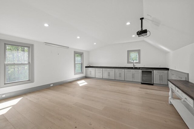 interior space with sink, gray cabinetry, light hardwood / wood-style floors, vaulted ceiling, and beverage cooler