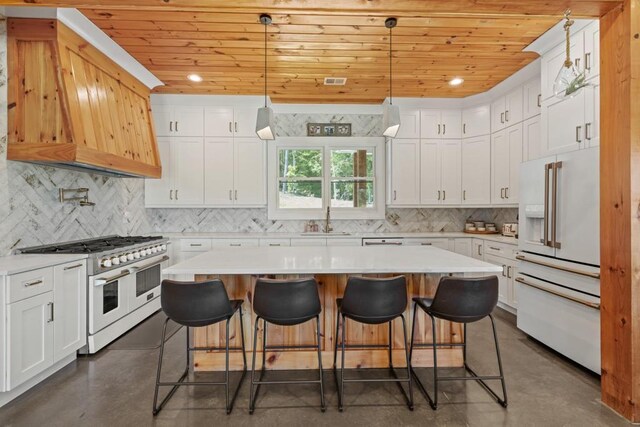 kitchen with a kitchen island, high quality appliances, sink, white cabinets, and hanging light fixtures