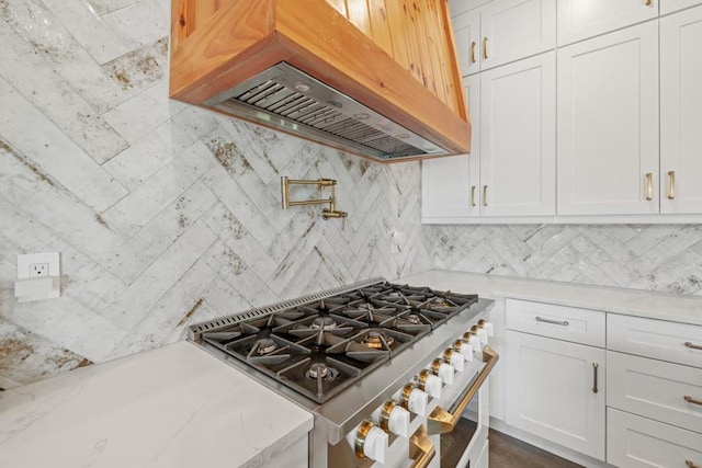 kitchen with white cabinetry, backsplash, high end stainless steel range, and premium range hood