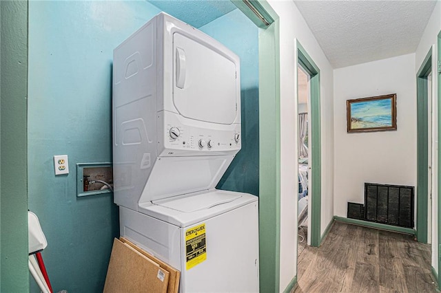 laundry area with stacked washer / drying machine, hardwood / wood-style flooring, and a textured ceiling