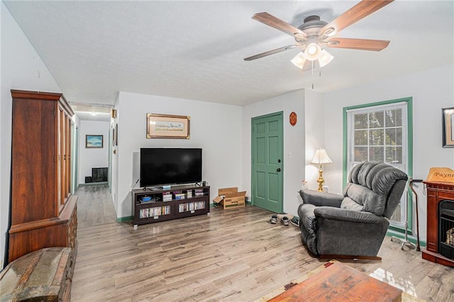 living room featuring a stone fireplace, a textured ceiling, light hardwood / wood-style floors, and ceiling fan