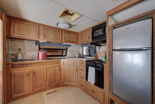 kitchen with visible vents, under cabinet range hood, light countertops, black appliances, and a sink