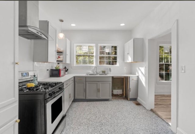 kitchen with gray cabinets, a healthy amount of sunlight, wall chimney range hood, and white range with gas stovetop