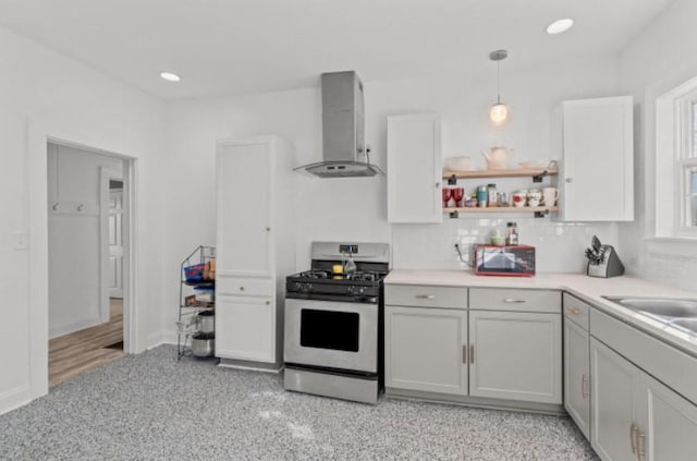 kitchen with gas stove, wall chimney exhaust hood, hanging light fixtures, tasteful backsplash, and white cabinets