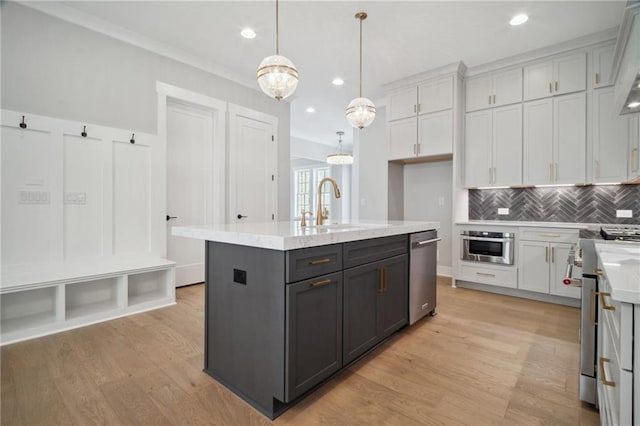 591 Brashy St, Woodstock, GA 30188 - kitchen featuring appliances with stainless steel finishes, light wood-style flooring, tasteful backsplash, a kitchen island with sink, and a sink