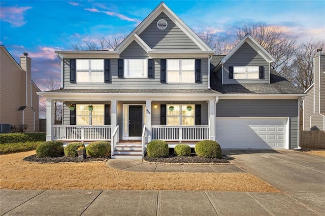 traditional home with an attached garage, covered porch, central AC, a shingled roof, and driveway