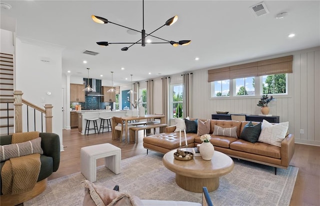 living area with light wood-style floors, visible vents, stairway, and an inviting chandelier