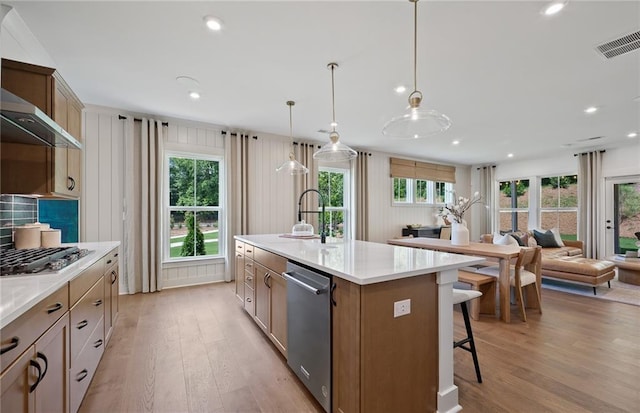 kitchen with light wood finished floors, visible vents, appliances with stainless steel finishes, wall chimney range hood, and a kitchen bar