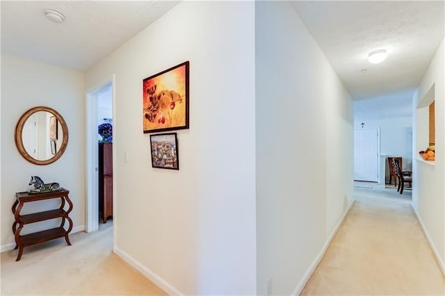 corridor featuring baseboards and light carpet