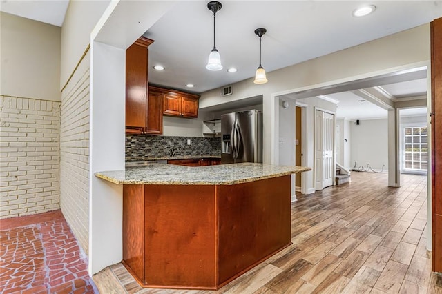 kitchen featuring light stone counters, brick wall, a peninsula, stainless steel fridge with ice dispenser, and light wood-style floors