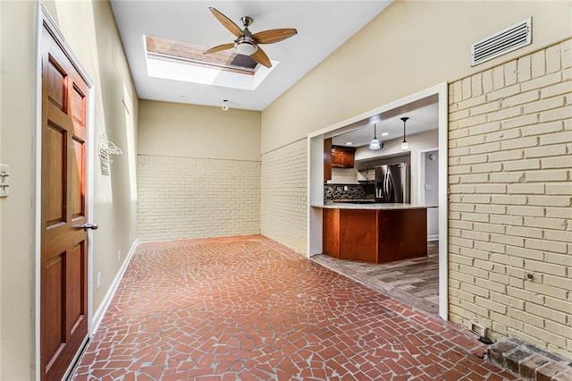 interior space with visible vents, stainless steel fridge, a skylight, brick wall, and brick floor