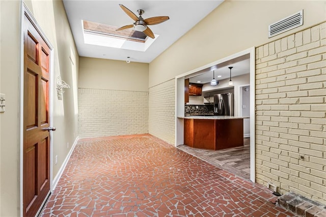 interior space featuring visible vents, baseboards, brick wall, and a skylight