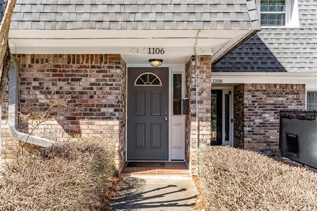 doorway to property featuring brick siding and a shingled roof