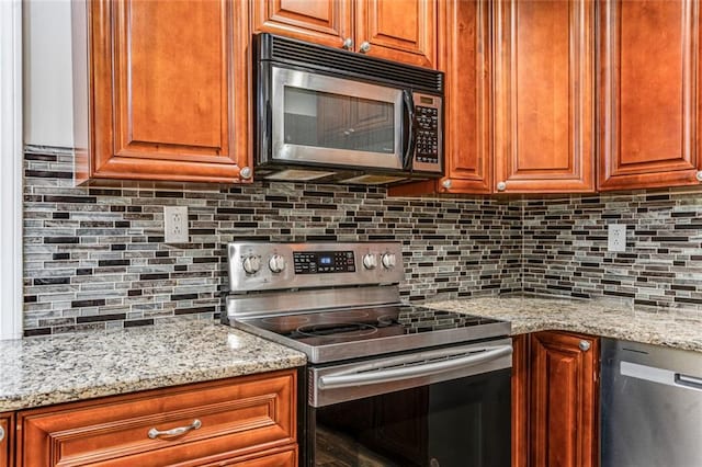 kitchen with backsplash, brown cabinets, appliances with stainless steel finishes, and light stone counters