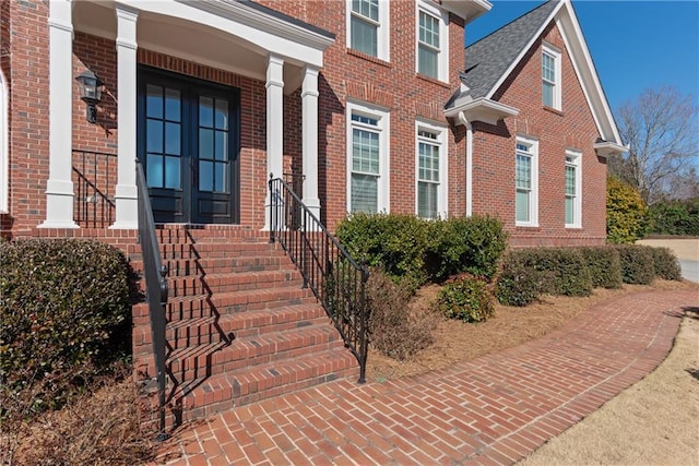 doorway to property featuring french doors, brick siding, and roof with shingles