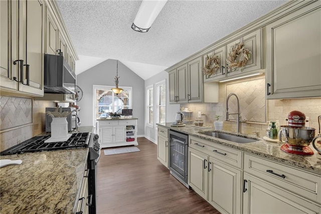 kitchen featuring beverage cooler, lofted ceiling, appliances with stainless steel finishes, cream cabinetry, and a sink