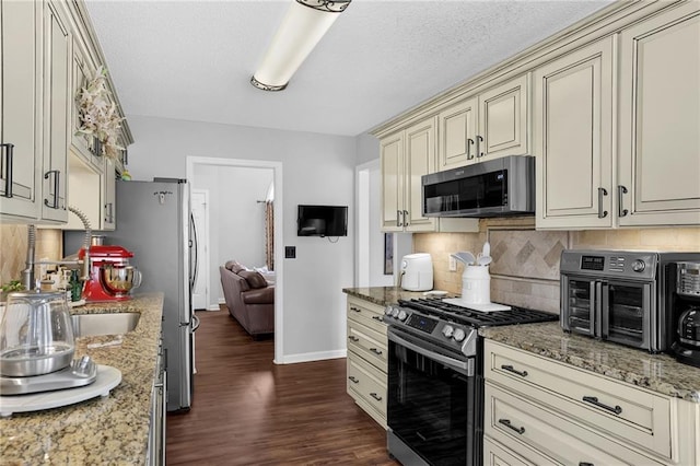 kitchen with dark wood-style floors, stainless steel appliances, backsplash, cream cabinets, and light stone countertops