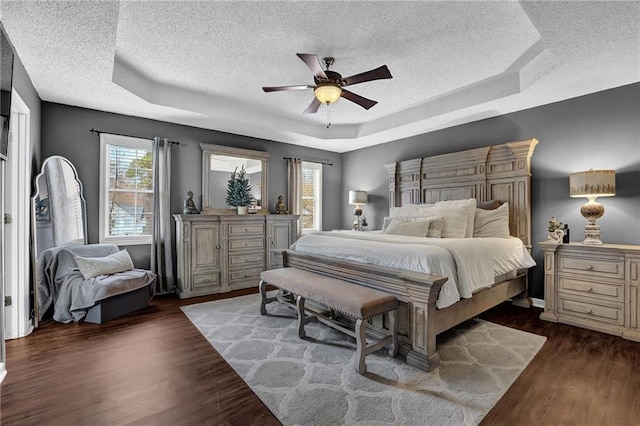 bedroom featuring a textured ceiling, a ceiling fan, a raised ceiling, and dark wood-type flooring