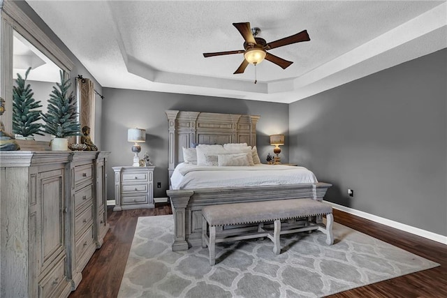 bedroom featuring baseboards, a raised ceiling, a ceiling fan, dark wood finished floors, and a textured ceiling