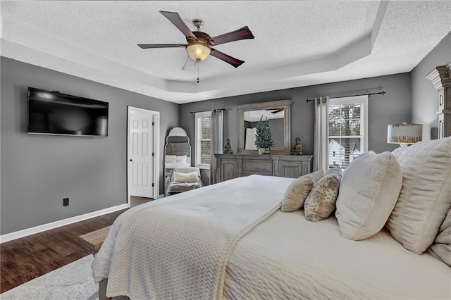 bedroom featuring baseboards, a ceiling fan, wood finished floors, a tray ceiling, and a textured ceiling