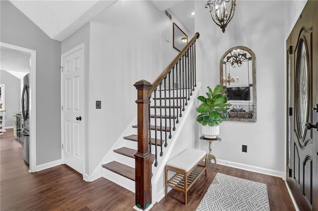 entryway with stairs, an inviting chandelier, baseboards, and wood finished floors