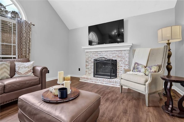 living area featuring vaulted ceiling, a brick fireplace, wood finished floors, and baseboards