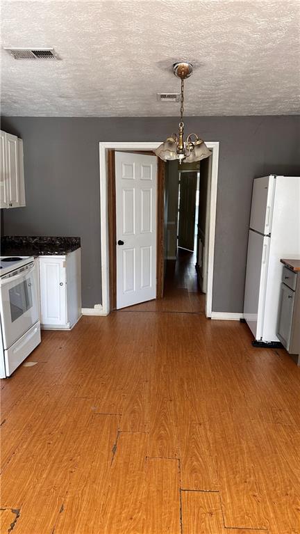 kitchen featuring hardwood / wood-style floors, pendant lighting, white cabinets, a notable chandelier, and white appliances