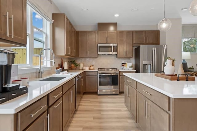 kitchen featuring sink, hanging light fixtures, stainless steel appliances, decorative backsplash, and light wood-type flooring