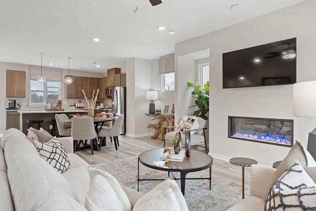 living room featuring ceiling fan, light wood-type flooring, and sink