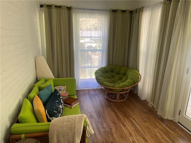 sitting room featuring a healthy amount of sunlight, brick wall, and hardwood / wood-style floors