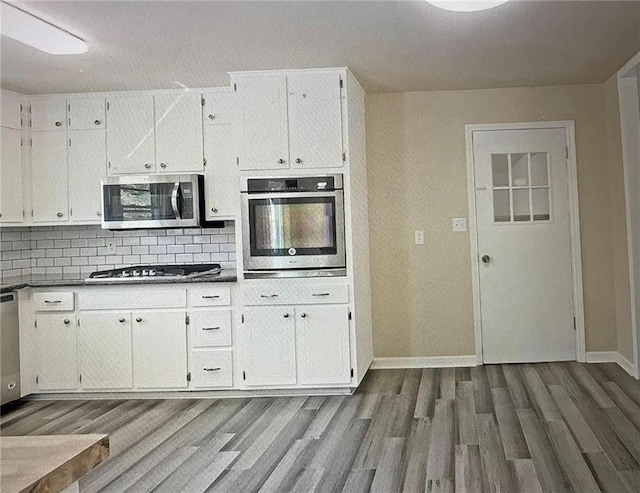 kitchen with appliances with stainless steel finishes, white cabinets, tasteful backsplash, and dark hardwood / wood-style flooring