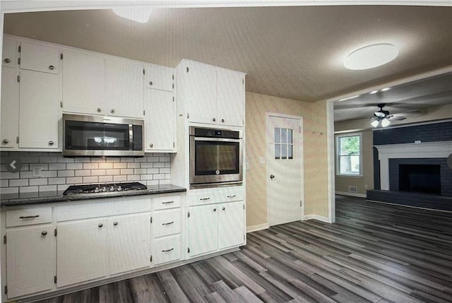 kitchen featuring ceiling fan, appliances with stainless steel finishes, white cabinetry, a brick fireplace, and dark hardwood / wood-style floors