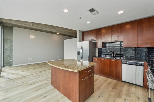 kitchen featuring stainless steel appliances, a sink, light wood-style flooring, tasteful backsplash, and a kitchen island