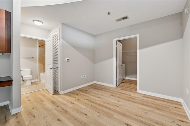 unfurnished bedroom with light wood-type flooring, baseboards, connected bathroom, and a walk in closet