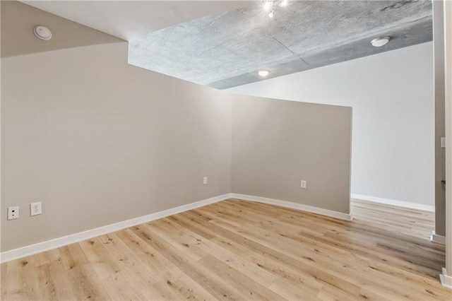 spare room with light wood-style floors, baseboards, a smoke detector, and lofted ceiling
