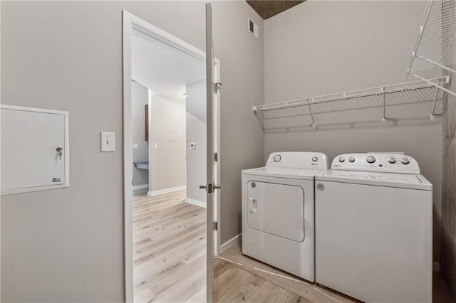 laundry area featuring separate washer and dryer, light wood-style flooring, and baseboards