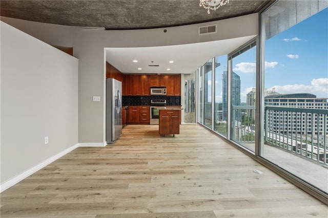 kitchen featuring appliances with stainless steel finishes, light wood-style flooring, decorative backsplash, baseboards, and a kitchen island