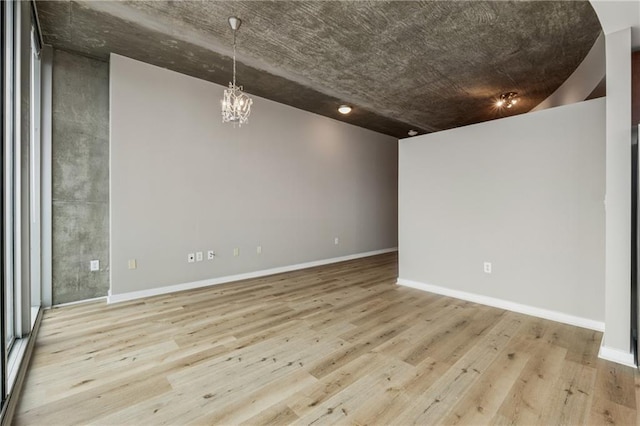 empty room with a chandelier, wood finished floors, and baseboards