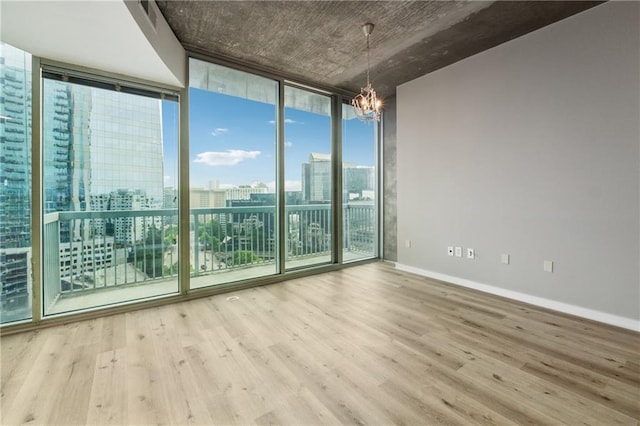 empty room featuring expansive windows, a chandelier, wood finished floors, a view of city, and baseboards
