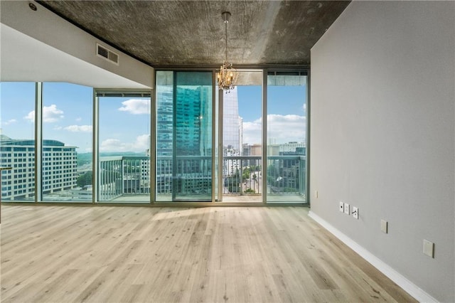 spare room featuring floor to ceiling windows, wood finished floors, a chandelier, a city view, and baseboards