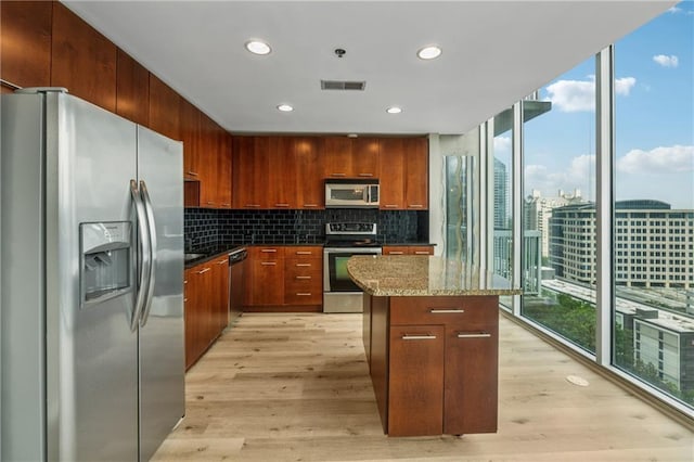 kitchen featuring appliances with stainless steel finishes, a kitchen island, backsplash, light wood-style floors, and dark stone countertops