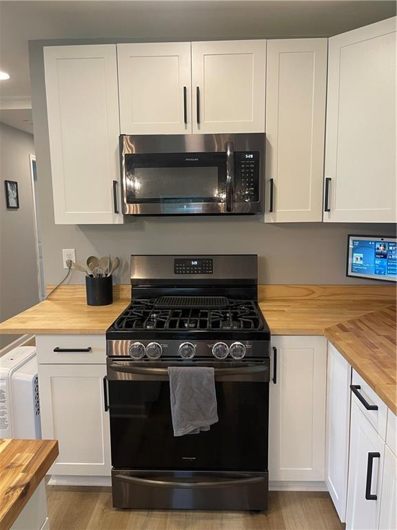 433 Spring Place Reseca Rd, Resaca, GA 30735 - kitchen with wood counters, stainless steel microwave, black gas range oven, white cabinets, and light wood finished floors