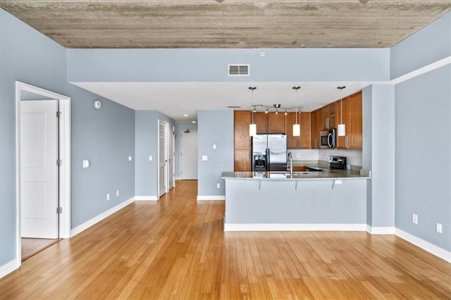 kitchen with pendant lighting, sink, appliances with stainless steel finishes, kitchen peninsula, and light wood-type flooring