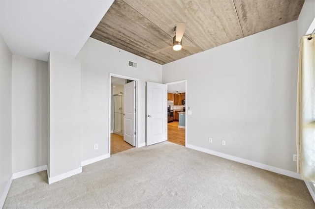 unfurnished bedroom featuring ensuite bath, stainless steel fridge, light colored carpet, and ceiling fan