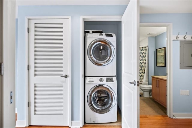 laundry room with stacked washer / dryer, electric panel, and light wood-type flooring