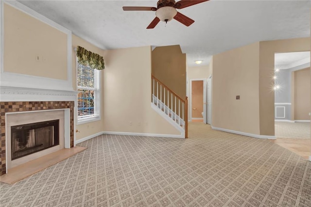 unfurnished living room featuring carpet, baseboards, stairway, a tile fireplace, and a ceiling fan