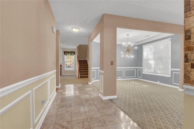 hallway with a notable chandelier, a decorative wall, stairway, and a wainscoted wall